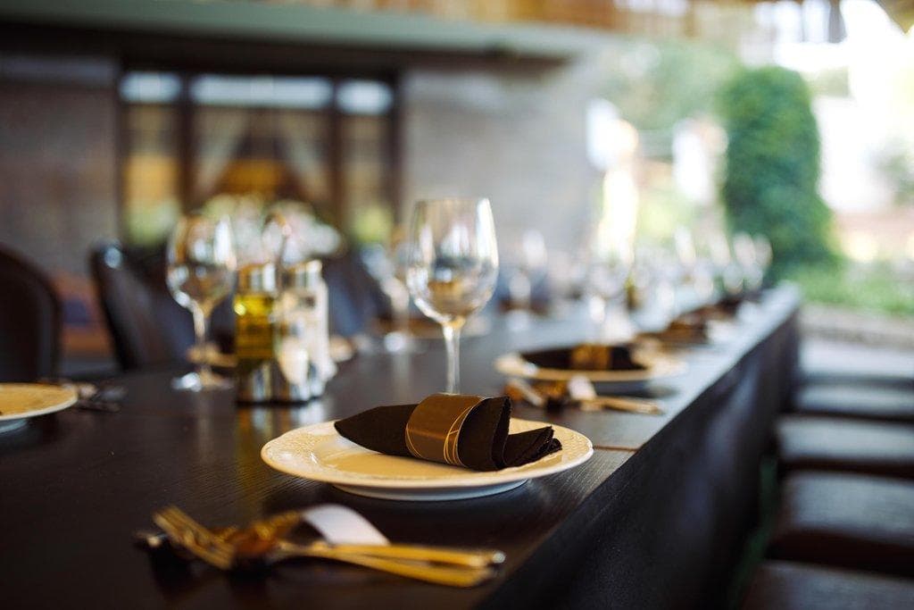 Elegant gedeckter langer Tisch mit Weingläsern, weißen Tellern und schwarzen Servietten in goldenen Ringen.