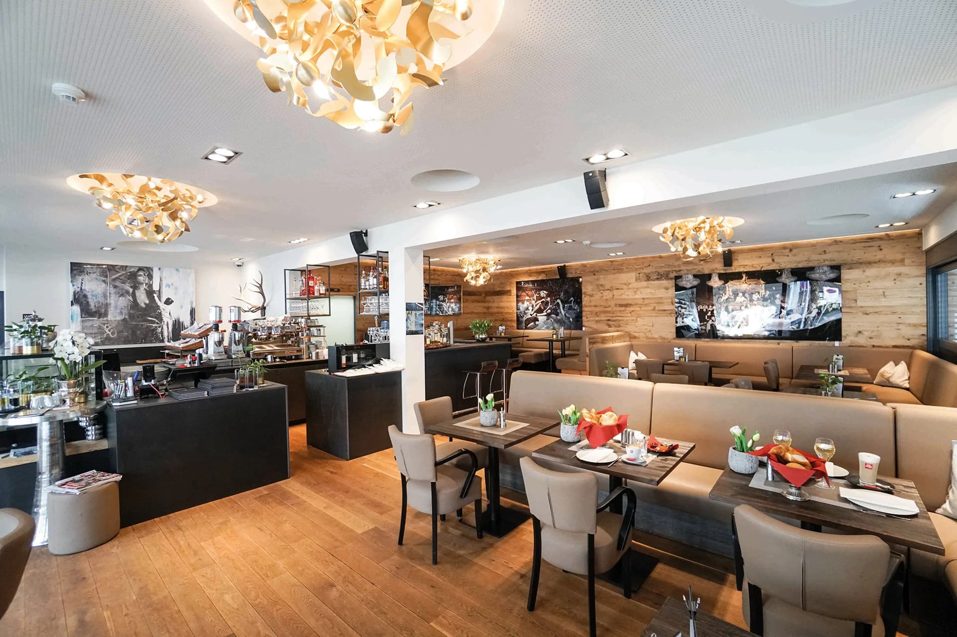 Platzhirsch Restaurant-Interieur mit hellen Holzböden, eleganten goldfarbenen Kronleuchtern und gemütlichen Sitzecken.